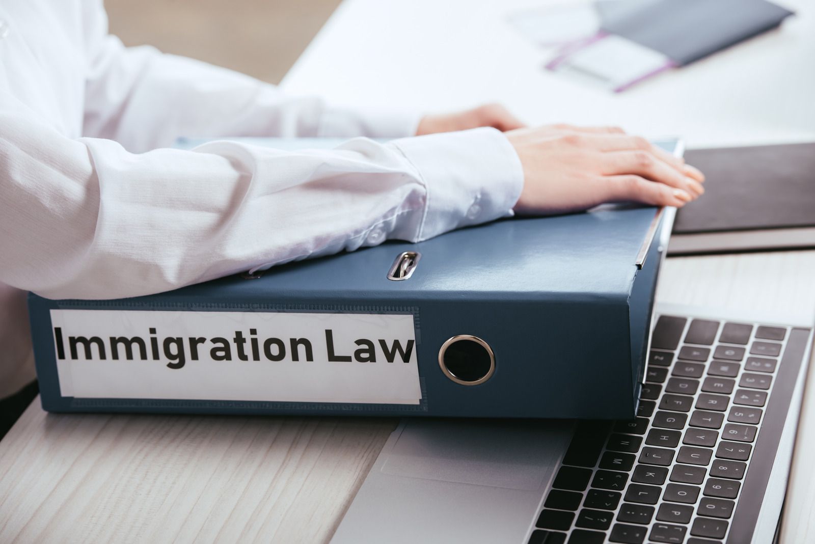 A person is sitting at a desk with a laptop and a binder with the word immigration law on it.