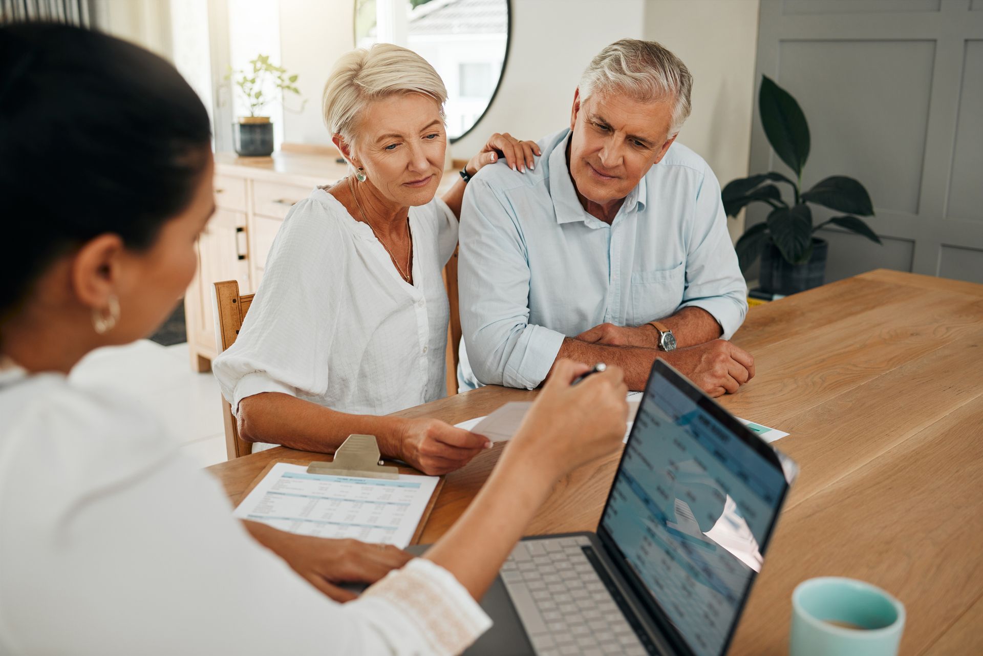 An elderly couple is sitting at a table looking at a laptop computer.