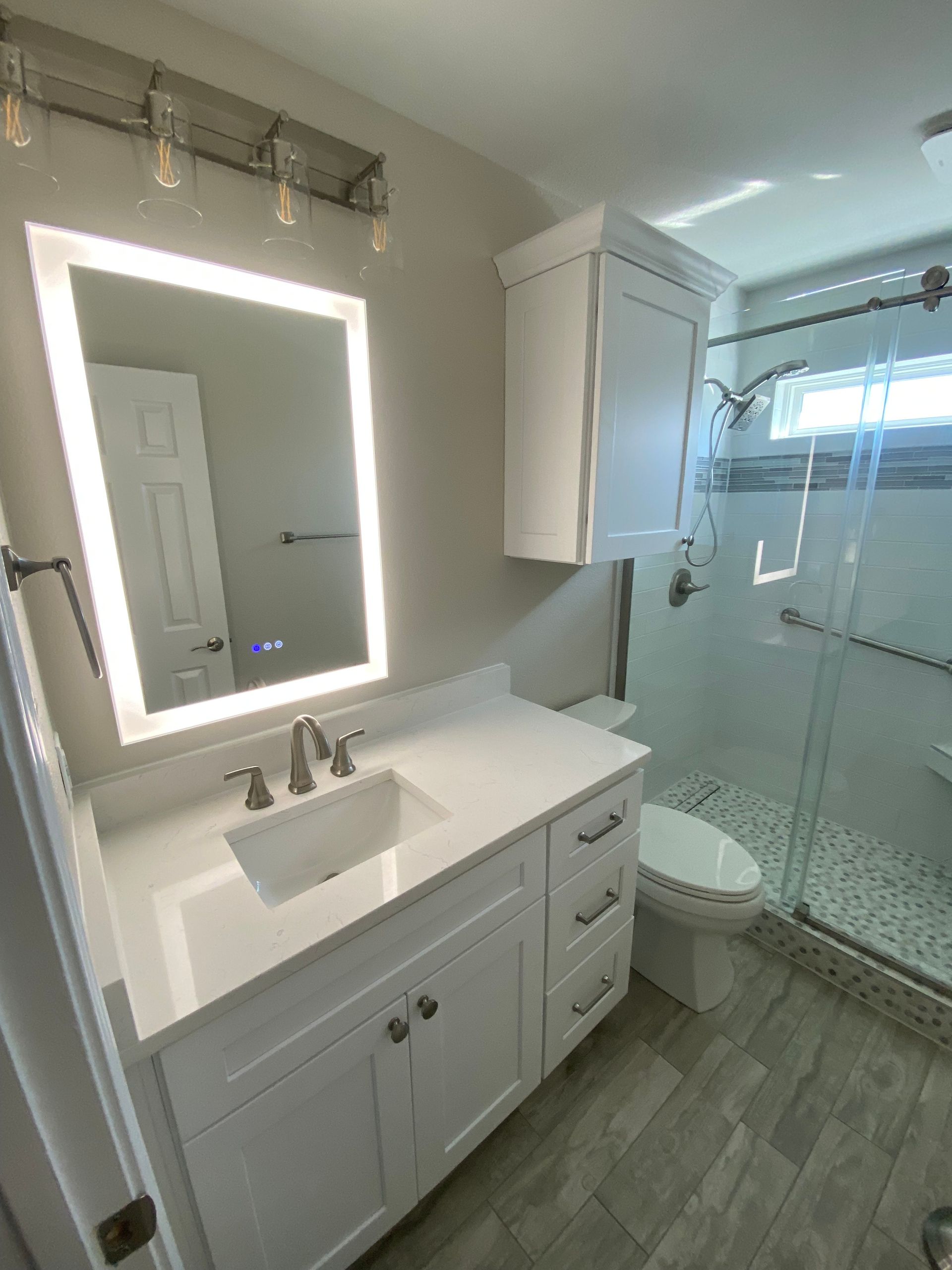 A bathroom with a sink , toilet , shower and mirror.