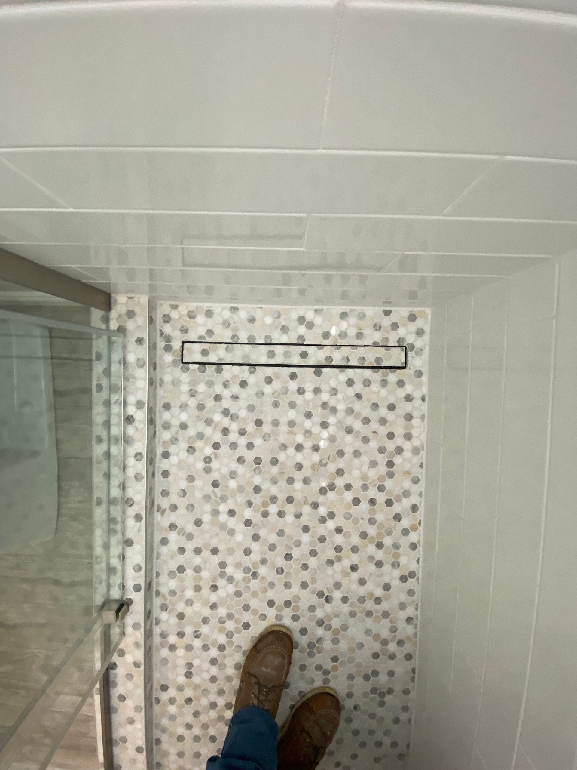 A person is standing in a shower with a mosaic tile wall.