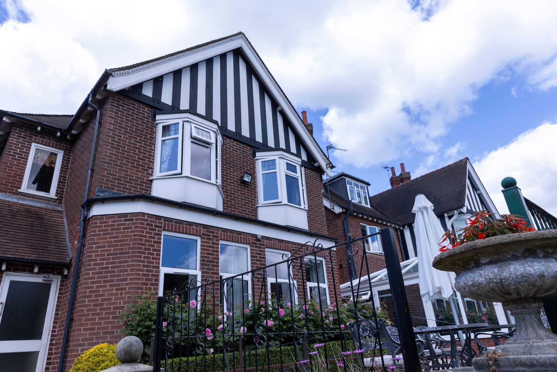 Two-story brick building with black and white gabled roof trim. Windows and a small water fountain in the foreground.