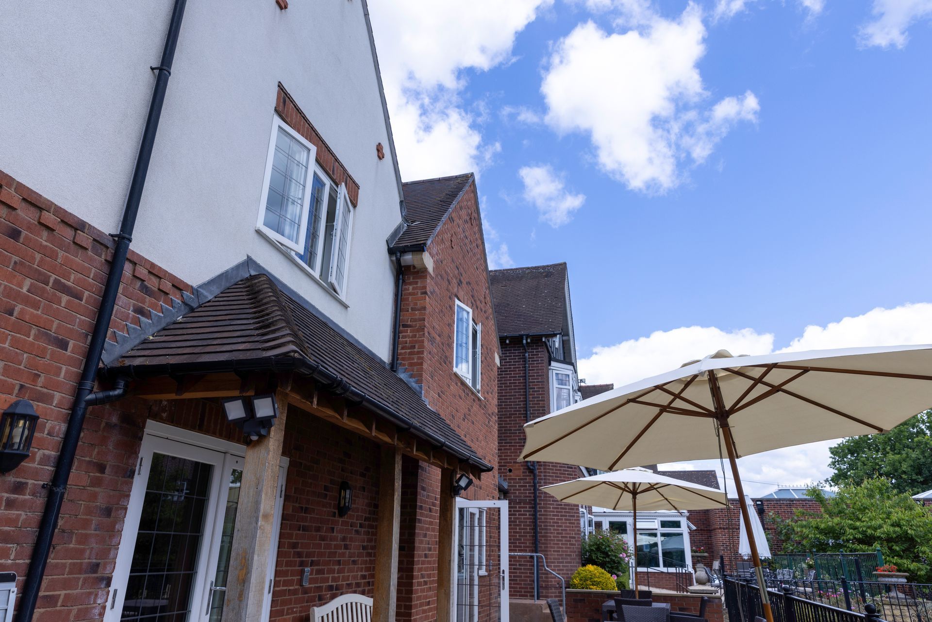 Exterior of a brick building with white trim and a porch, featuring an umbrella, under a blue sky.