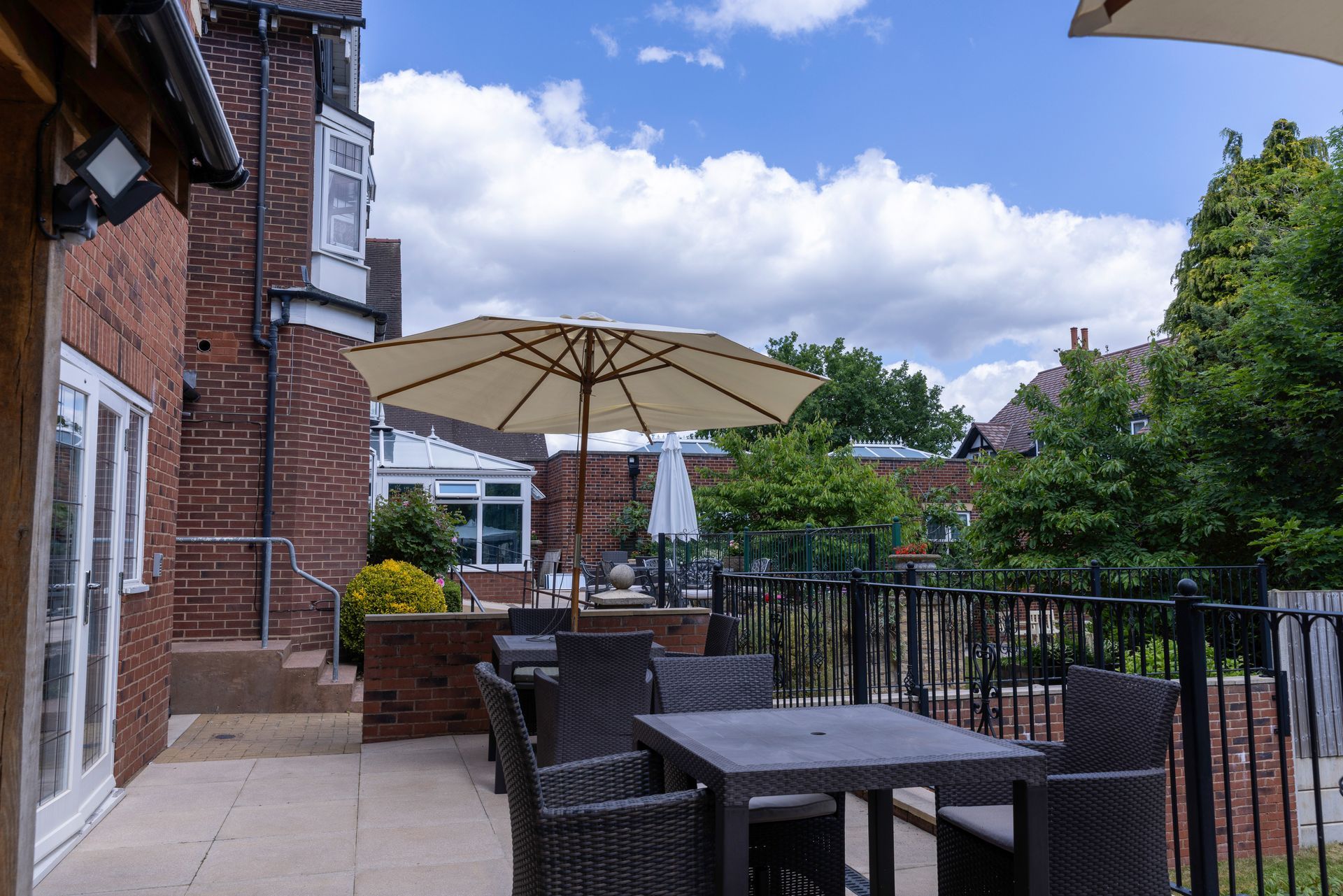 Outdoor patio with tables, chairs, and an umbrella in front of a brick building under a cloudy sky.