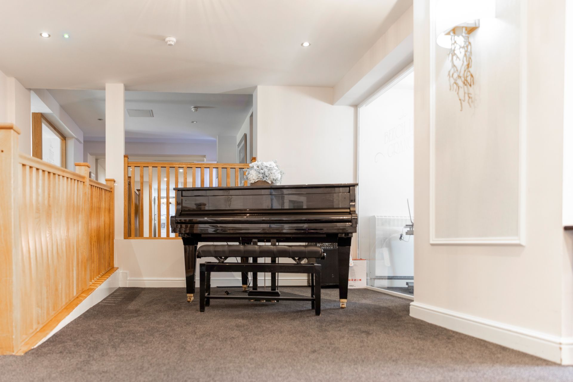 A black piano and bench in a brightly lit room with gray carpet and light wood accents.
