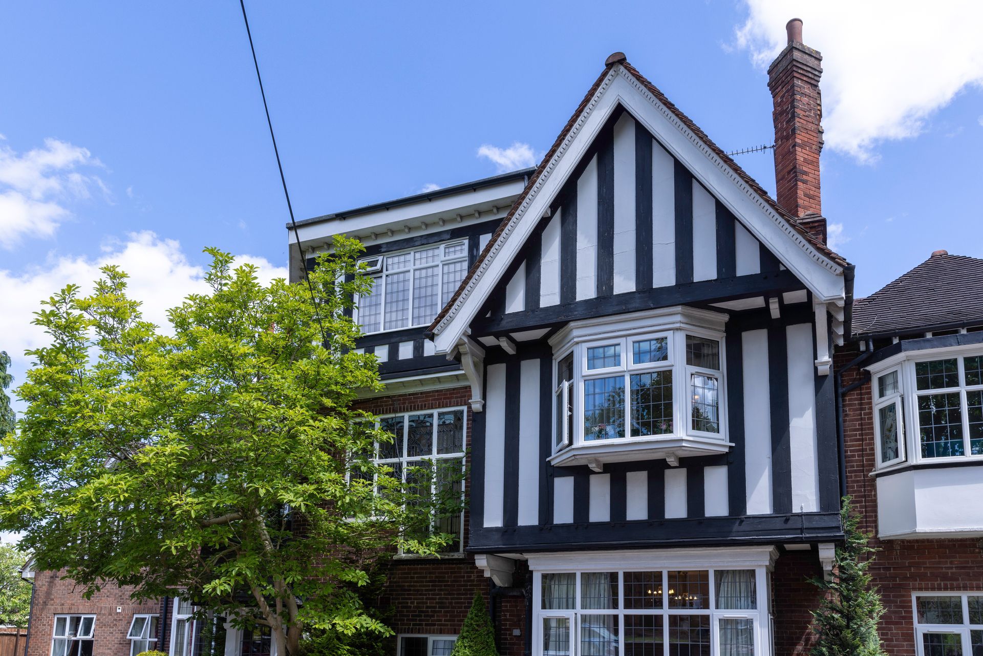 Black and white Tudor-style house with a bay window. A green tree is on the left side of the house. Blue sky.
