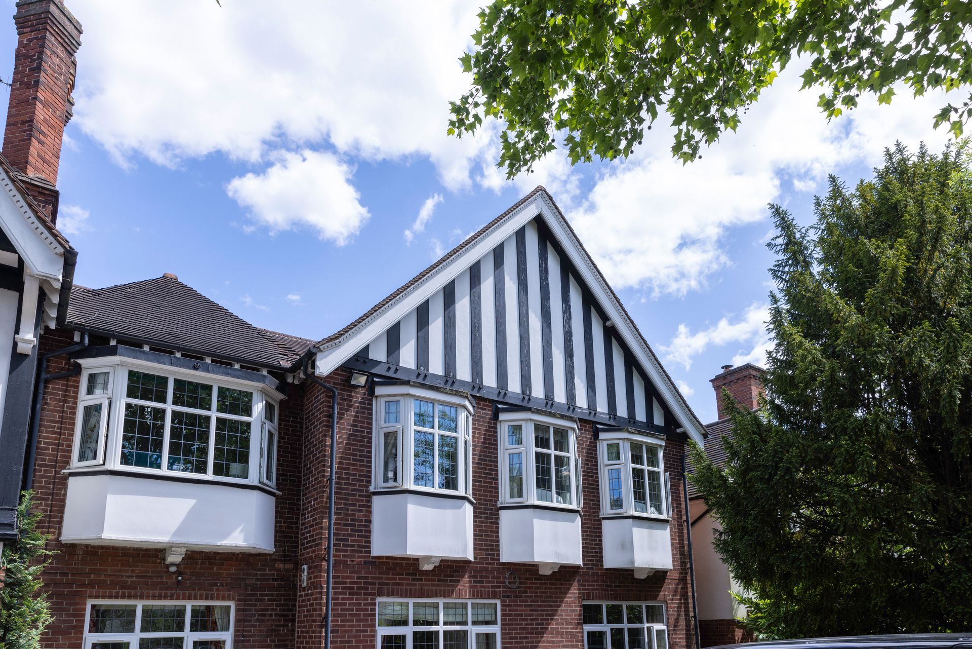 Brick house with bay windows and a black and white striped gable under a blue sky.