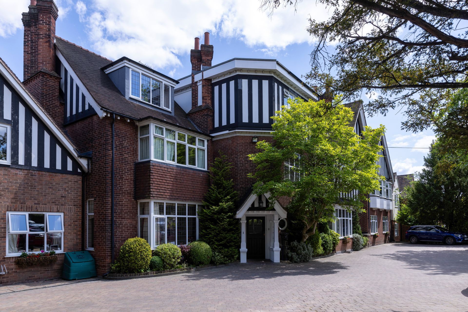 Brick building with black and white trim and several windows, with a paved driveway and some trees.