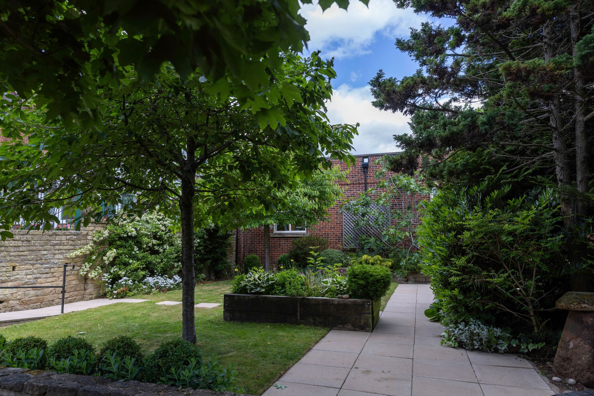 A serene garden with a tree, brick building in the background, and a stone pathway.