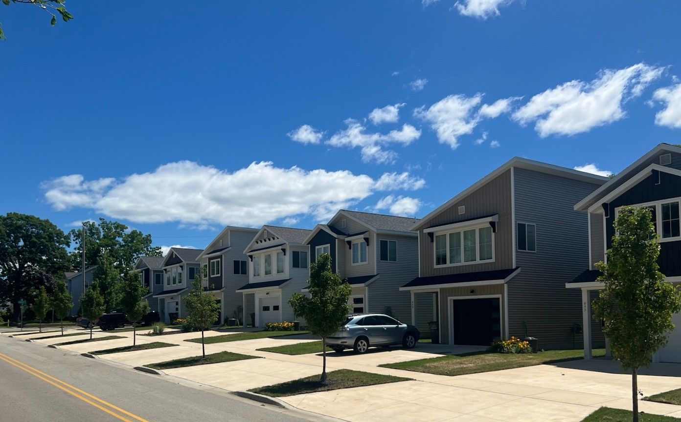 A row of houses with cars parked in front of them on a sunny day.
