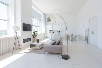 A modern, minimalist open-plan living room with white walls, a gray sofa, a coffee table, and a large arched floor lamp.