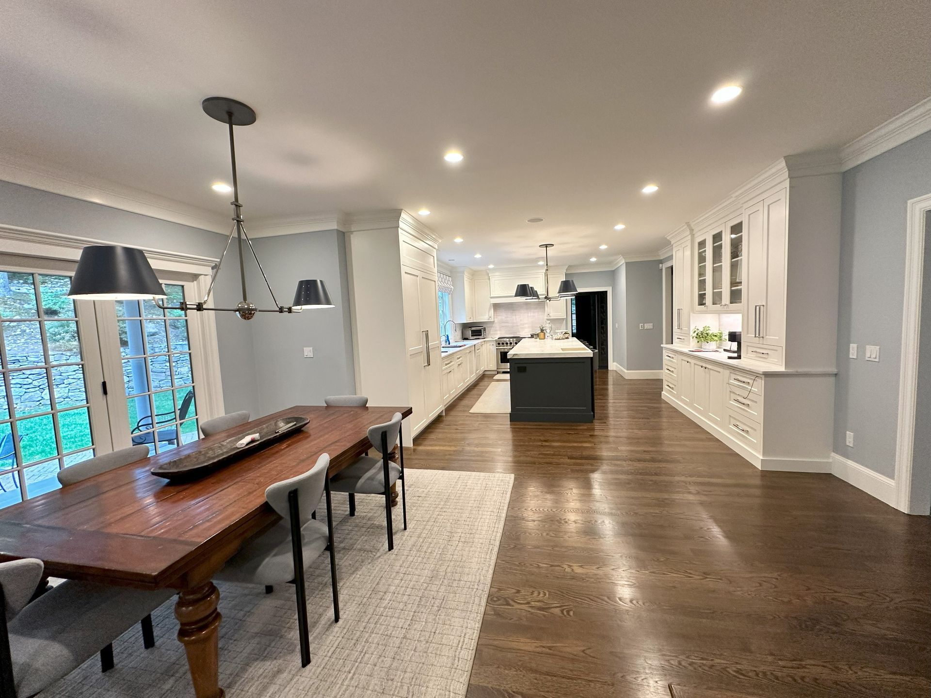 A dining room with a wooden table and chairs and a kitchen in the background.
