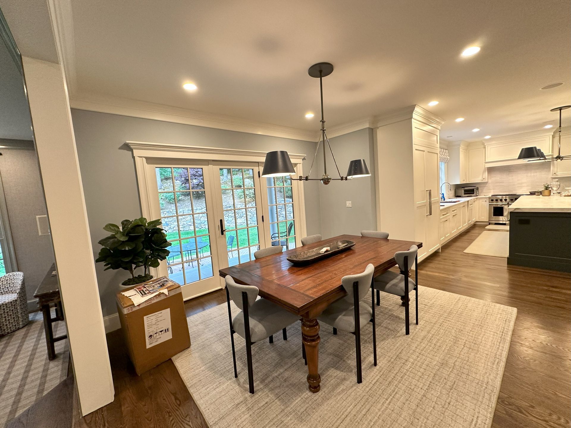 A dining room with a wooden table and chairs and a kitchen in the background.