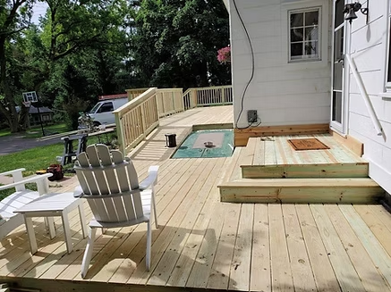 A wooden deck with chairs and a table in front of a white house.