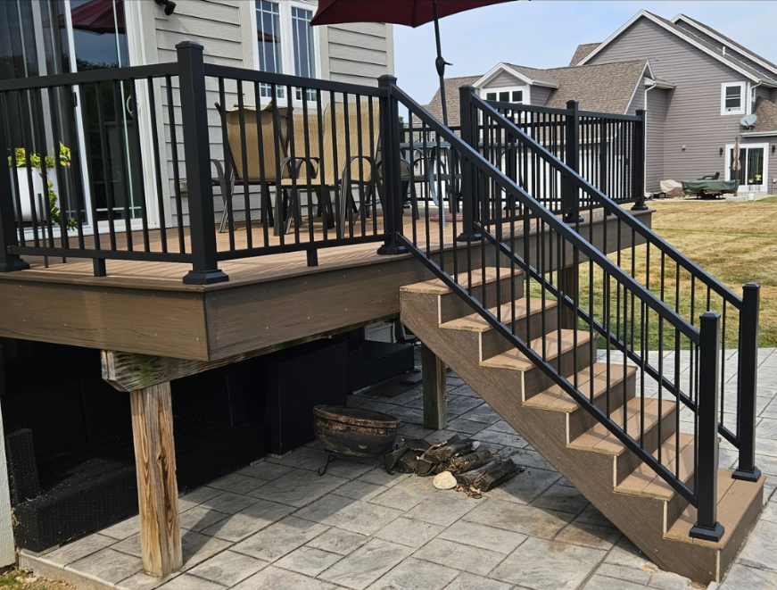 A deck with stairs leading up to it and a black railing.