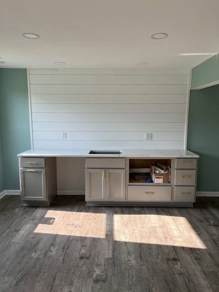 A kitchen with white cabinets , a sink , and a wooden floor.