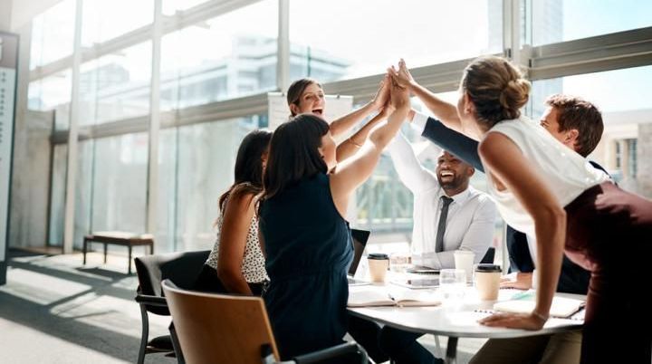 A group of people are giving each other a high five while sitting around a table.