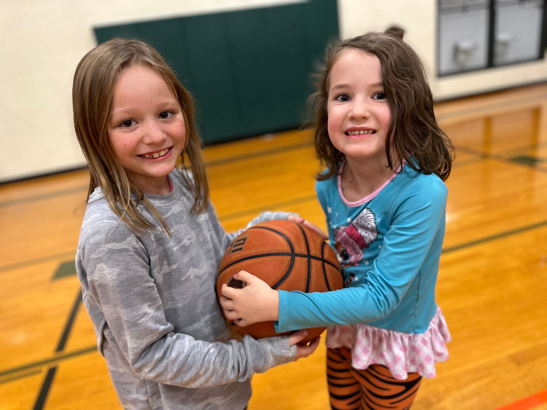 Two young girls are holding a basketball on a basketball court.