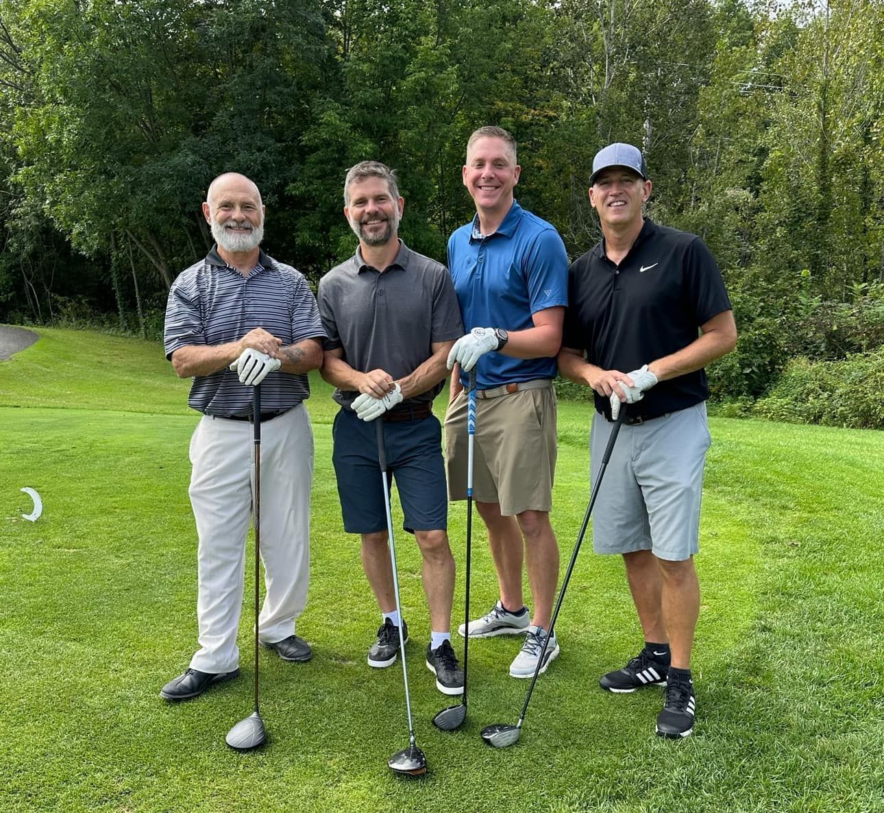 A group of men are standing on a golf course holding golf clubs.