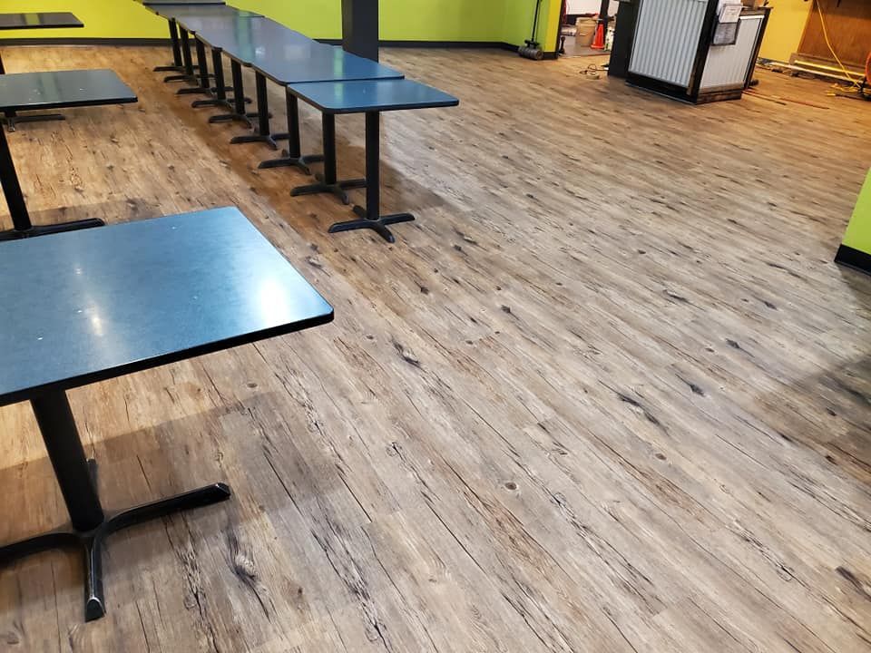 A row of tables are lined up on a wooden floor in a restaurant.