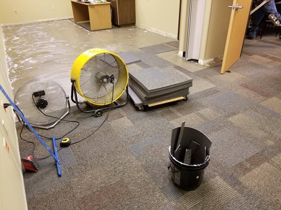 A room with a fan and a bucket on the floor.