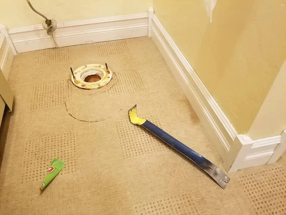 A tool is laying on the floor next to a toilet.