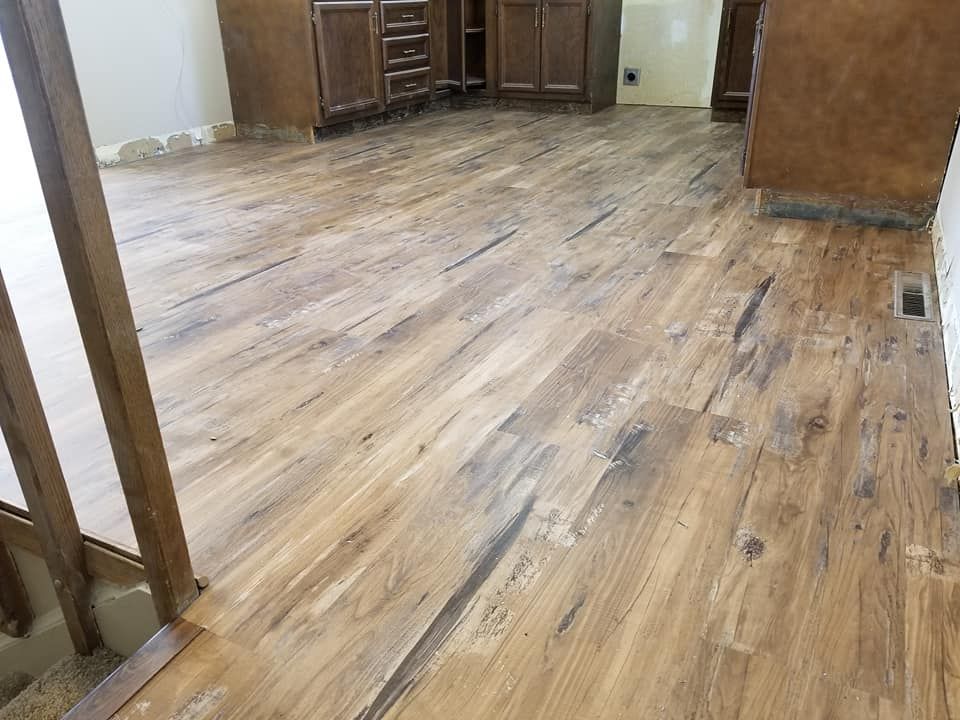 A room with a wooden floor and stairs leading to a kitchen.
