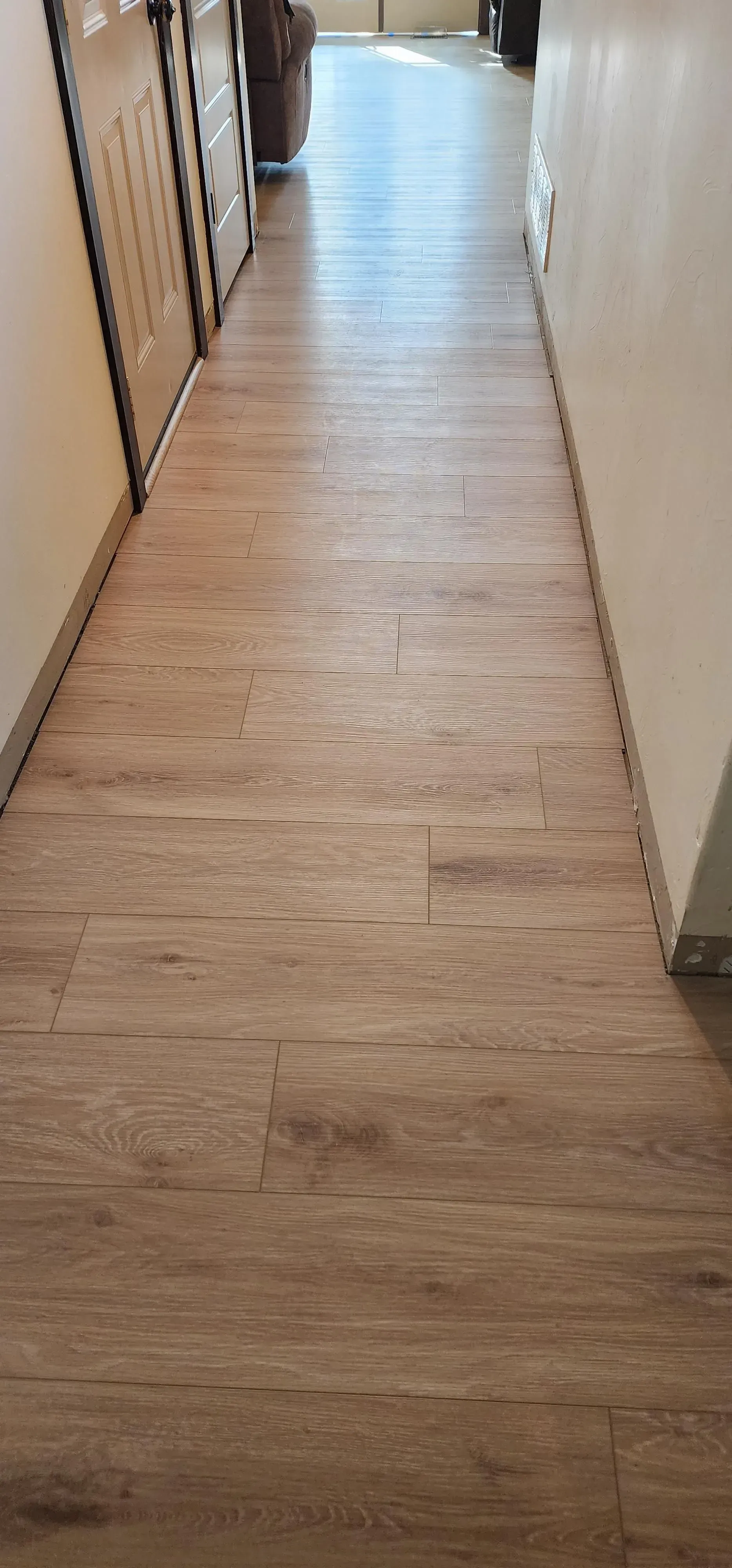 A hallway with a wooden floor and a couch in the background.