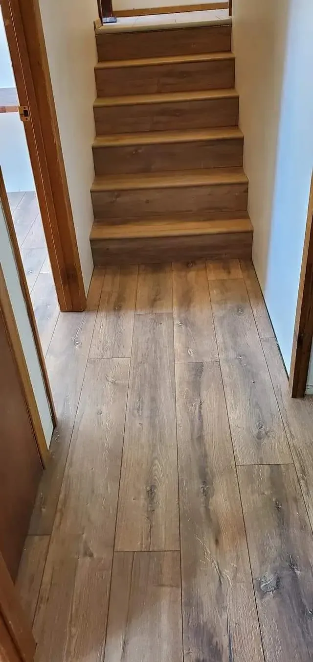 A hallway with wooden floors and stairs in a house.