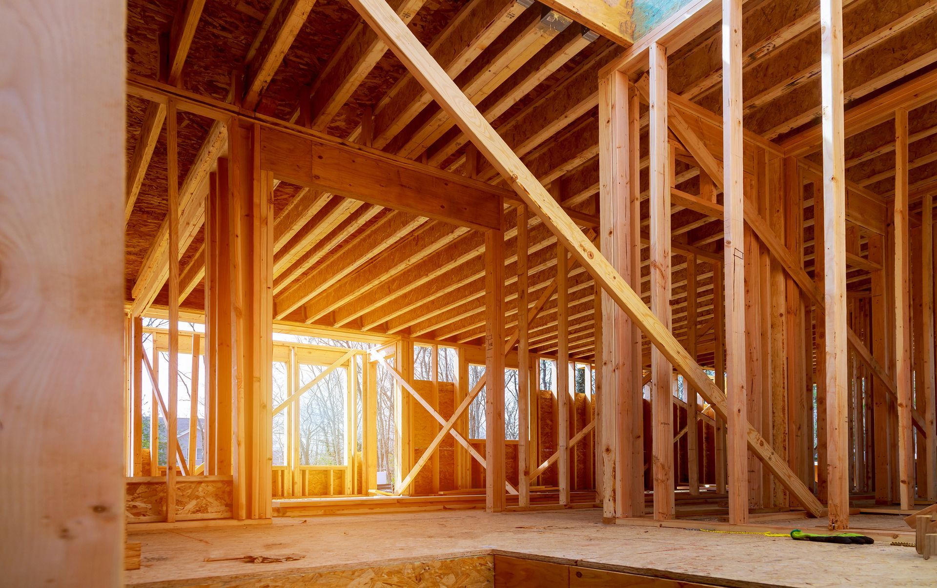 Wooden framing of a house under construction, interior view with natural light streaming in.