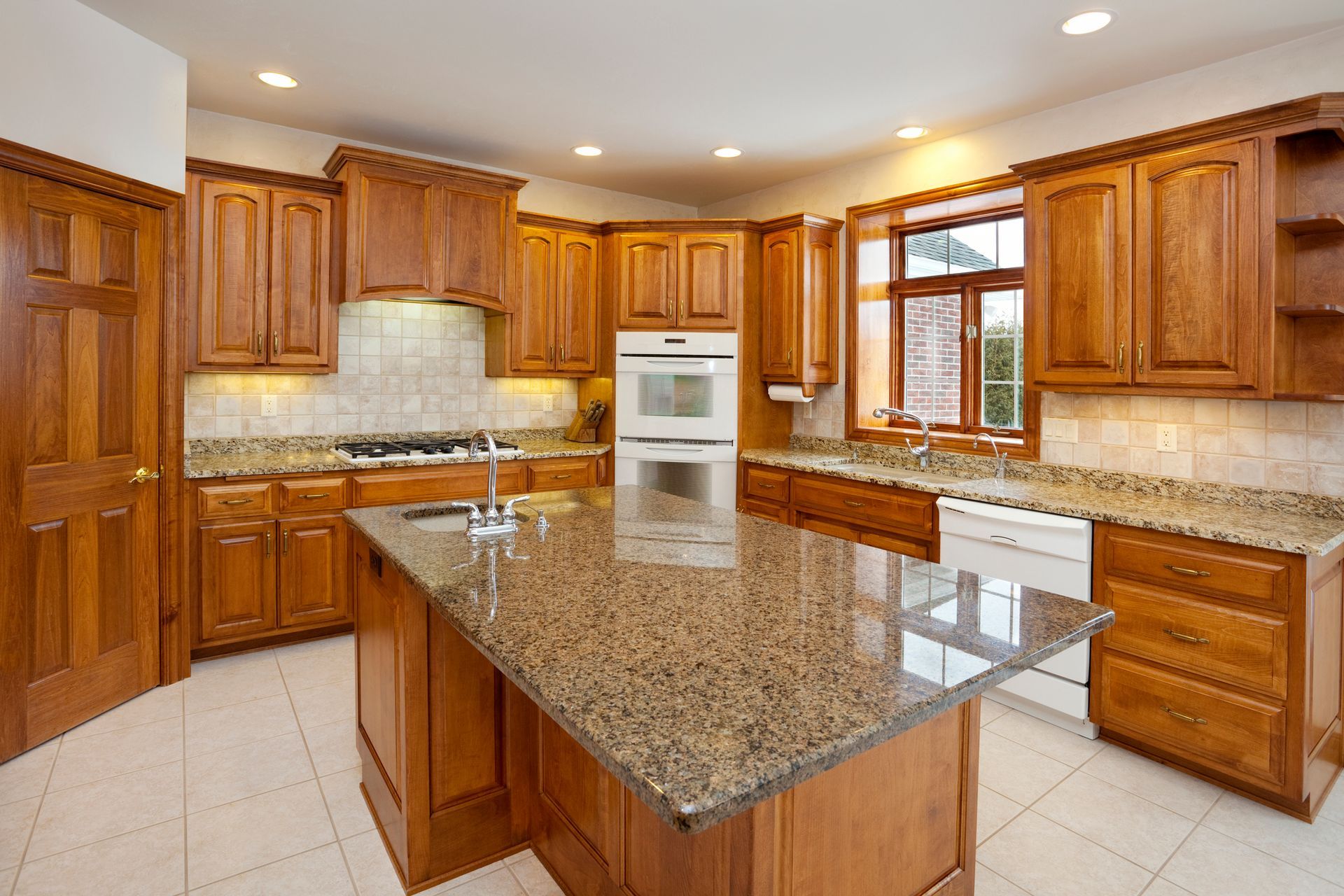 Kitchen with wood cabinets, granite countertops, island, and white appliances.