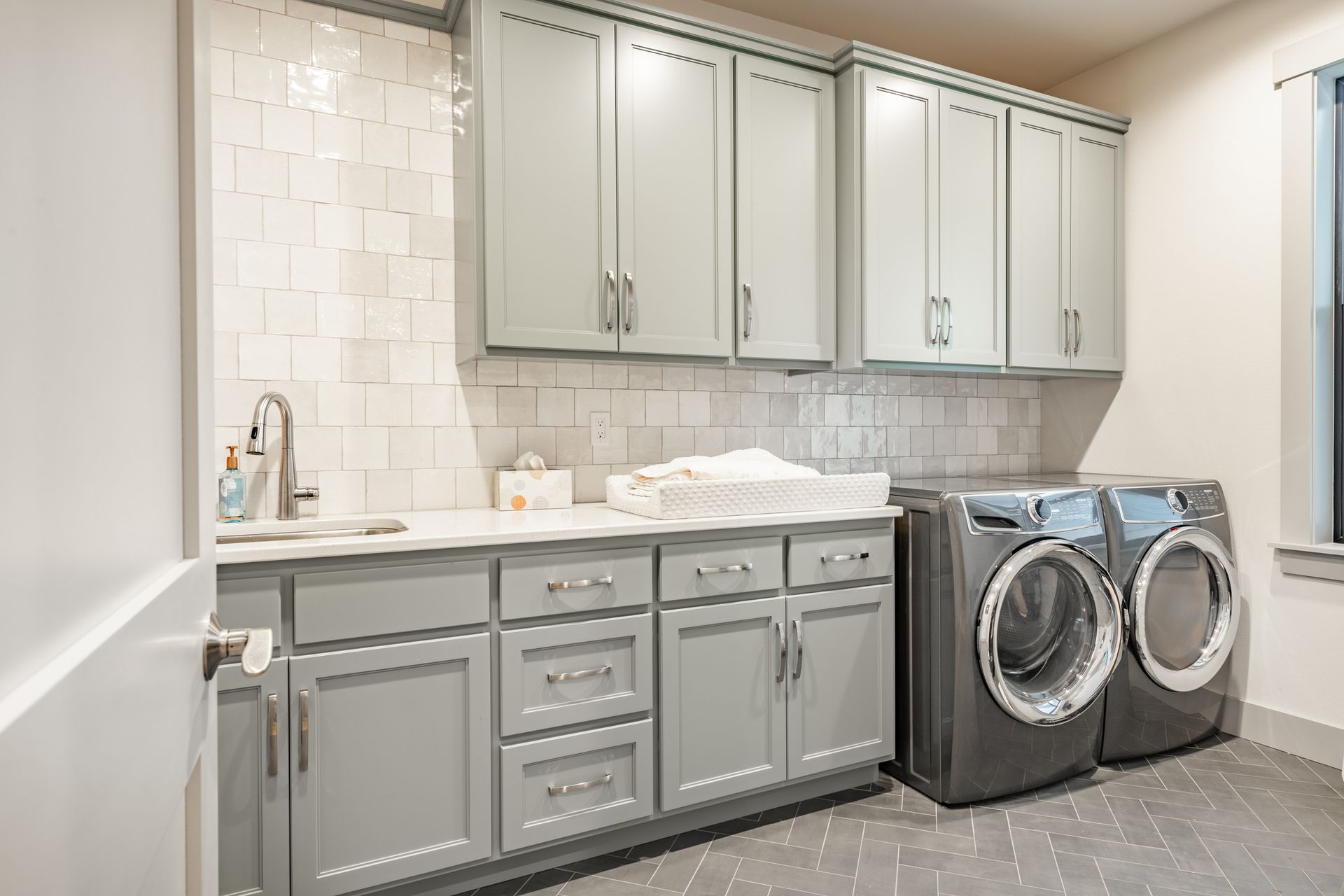 Laundry room with gray cabinets, white countertop, washing machine, and gray tile floor.