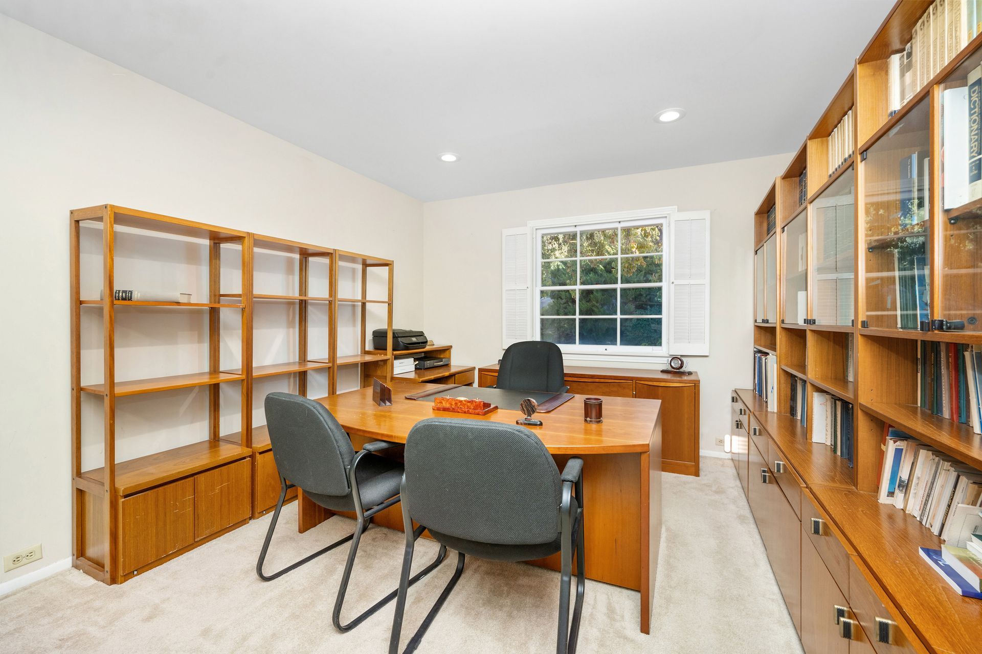 Home office with wooden desk, chairs, bookshelves, and a window with a view.