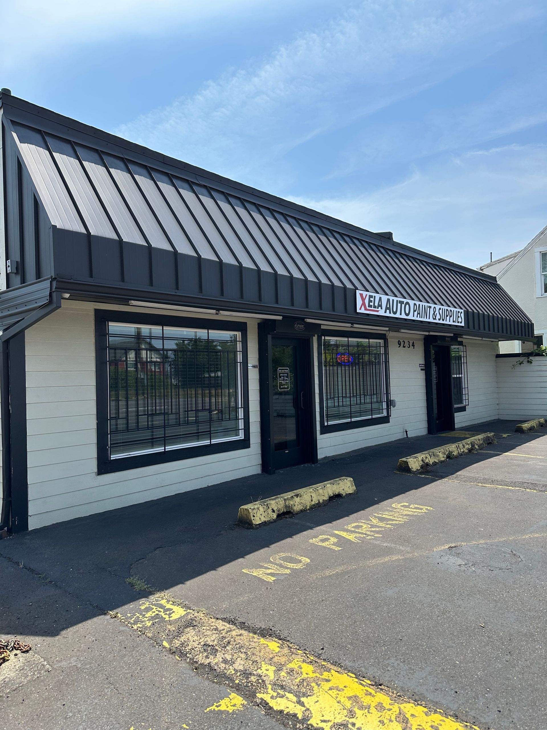Storefront with black awning and white walls, with windows and a door, in an asphalt parking area.