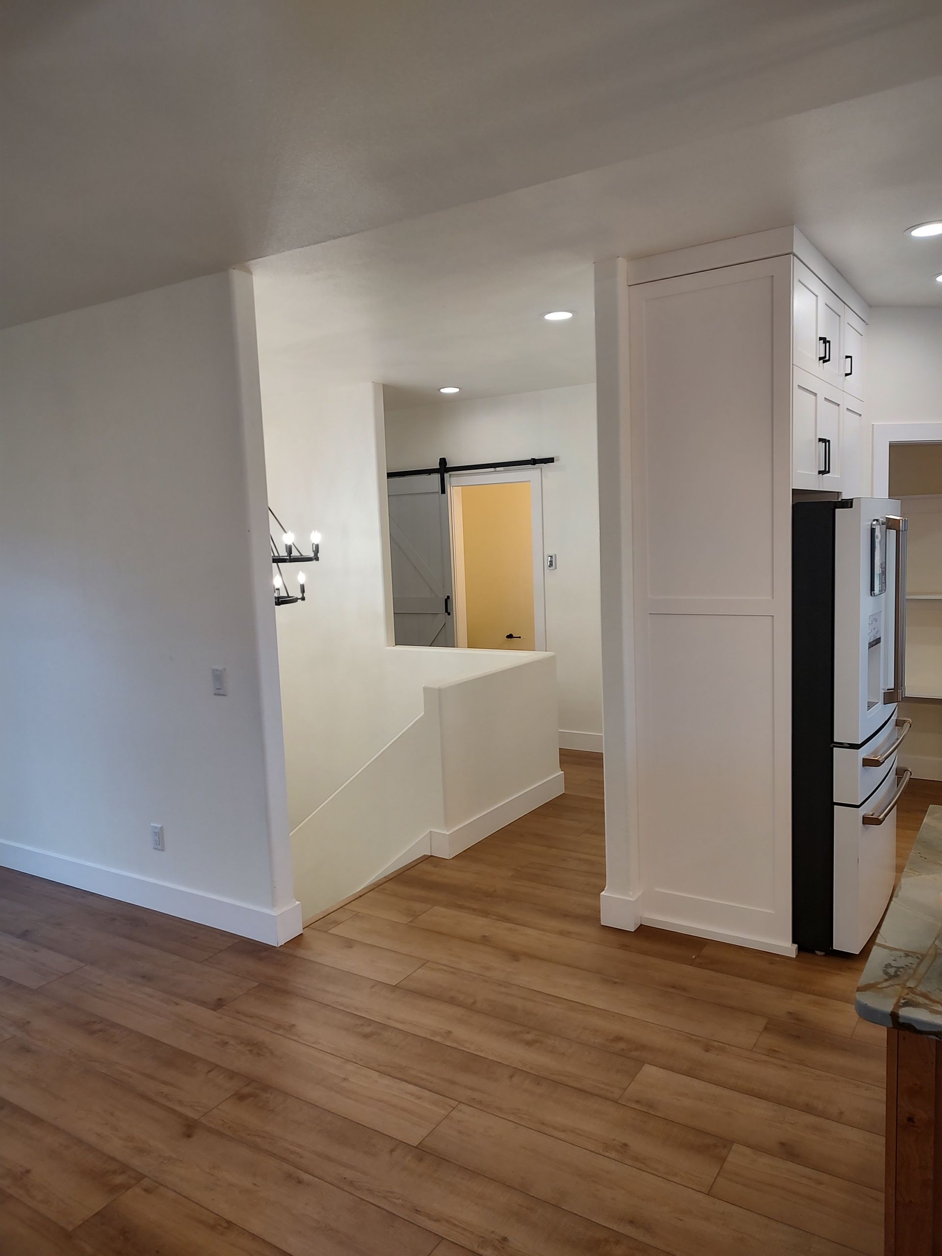 A kitchen with hardwood floors , white cabinets and a refrigerator.