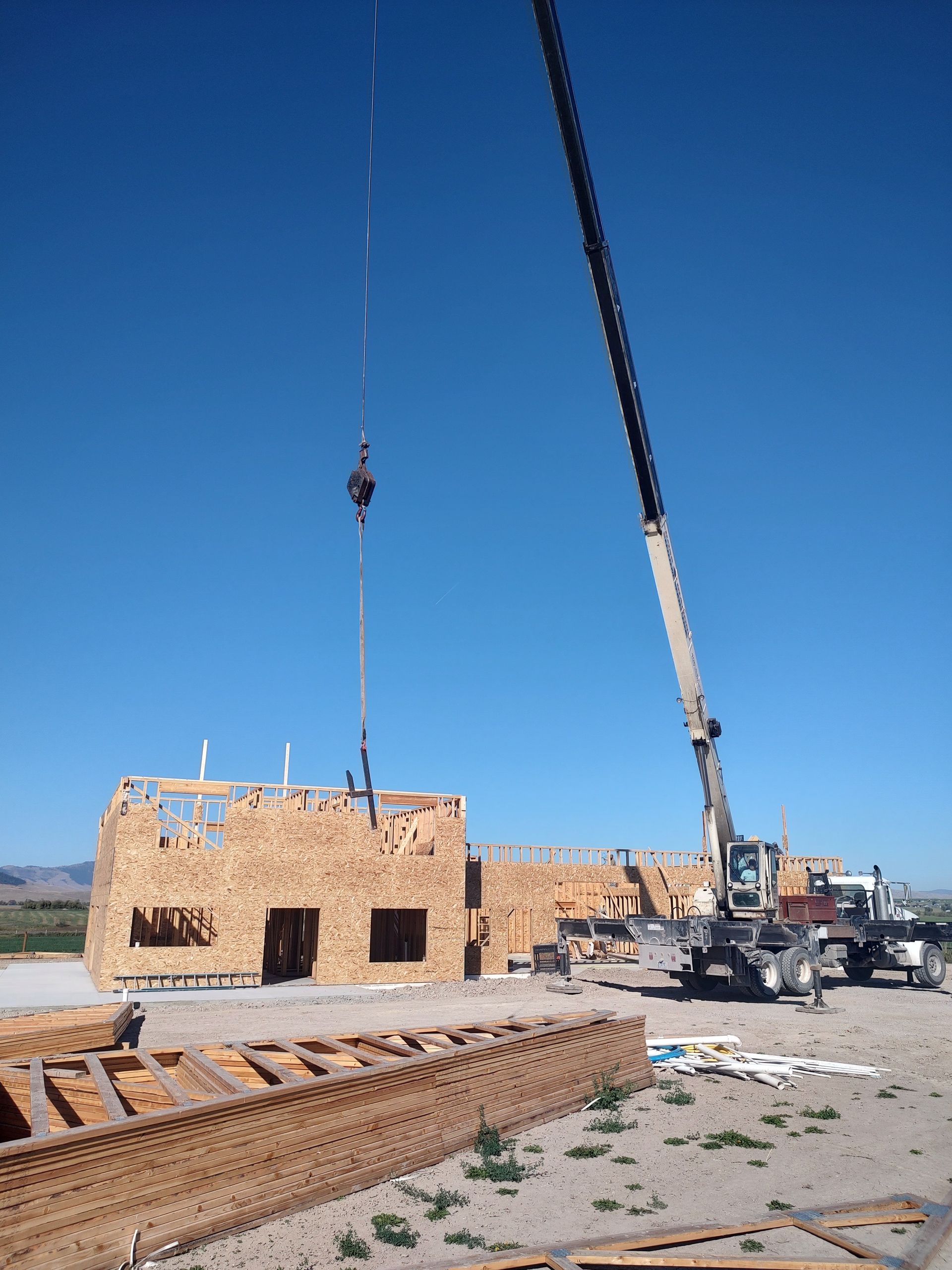 A crane is lifting a piece of wood in front of a building under construction