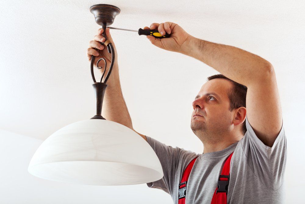 A Man Is Fixing a Light Fixture with A Screwdriver — Jason Wenta Electrical Services in Condon, QLD