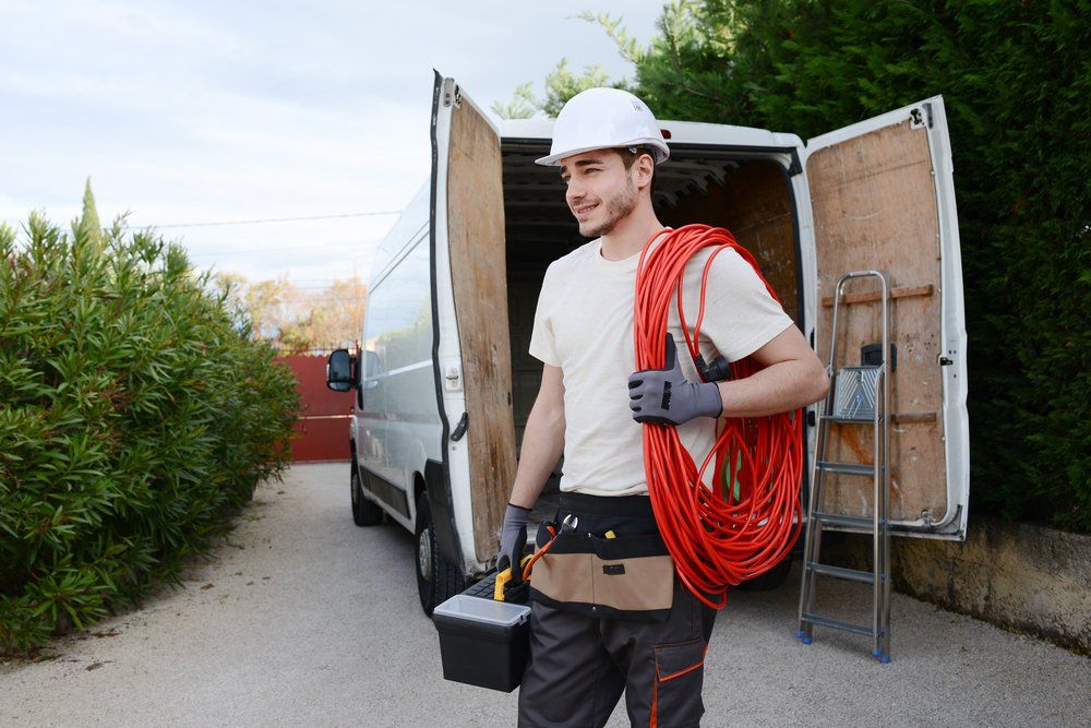 A Man Is Carrying a Hose and A Toolbox in Front of A Van — Jason Wenta Electrical Services in Condon, QLD