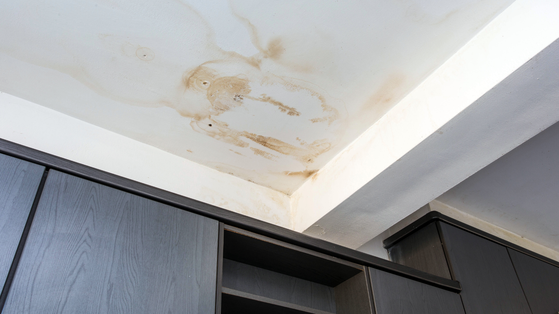 A ceiling with water stains on it in a room with cabinets.