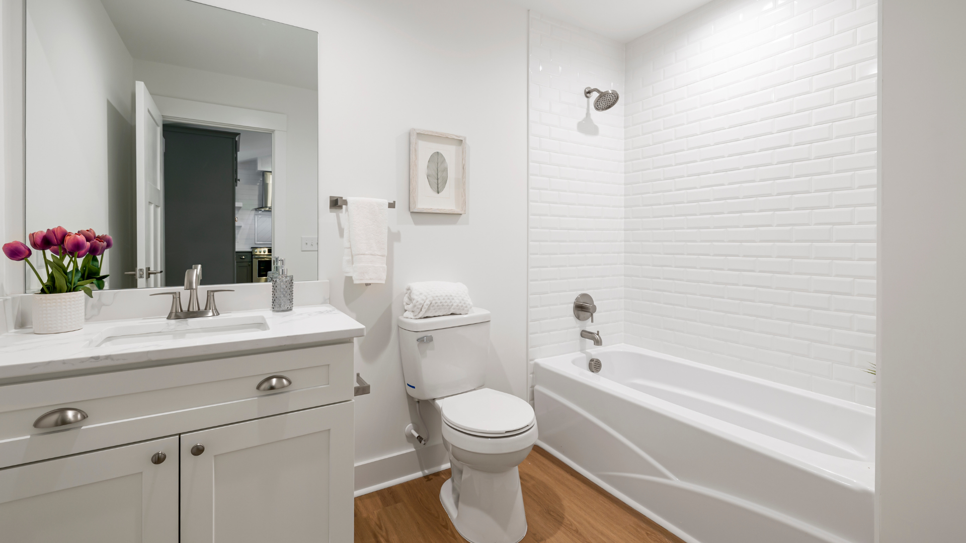 White bathroom with a bathtub, toilet, vanity, and a wooden floor.