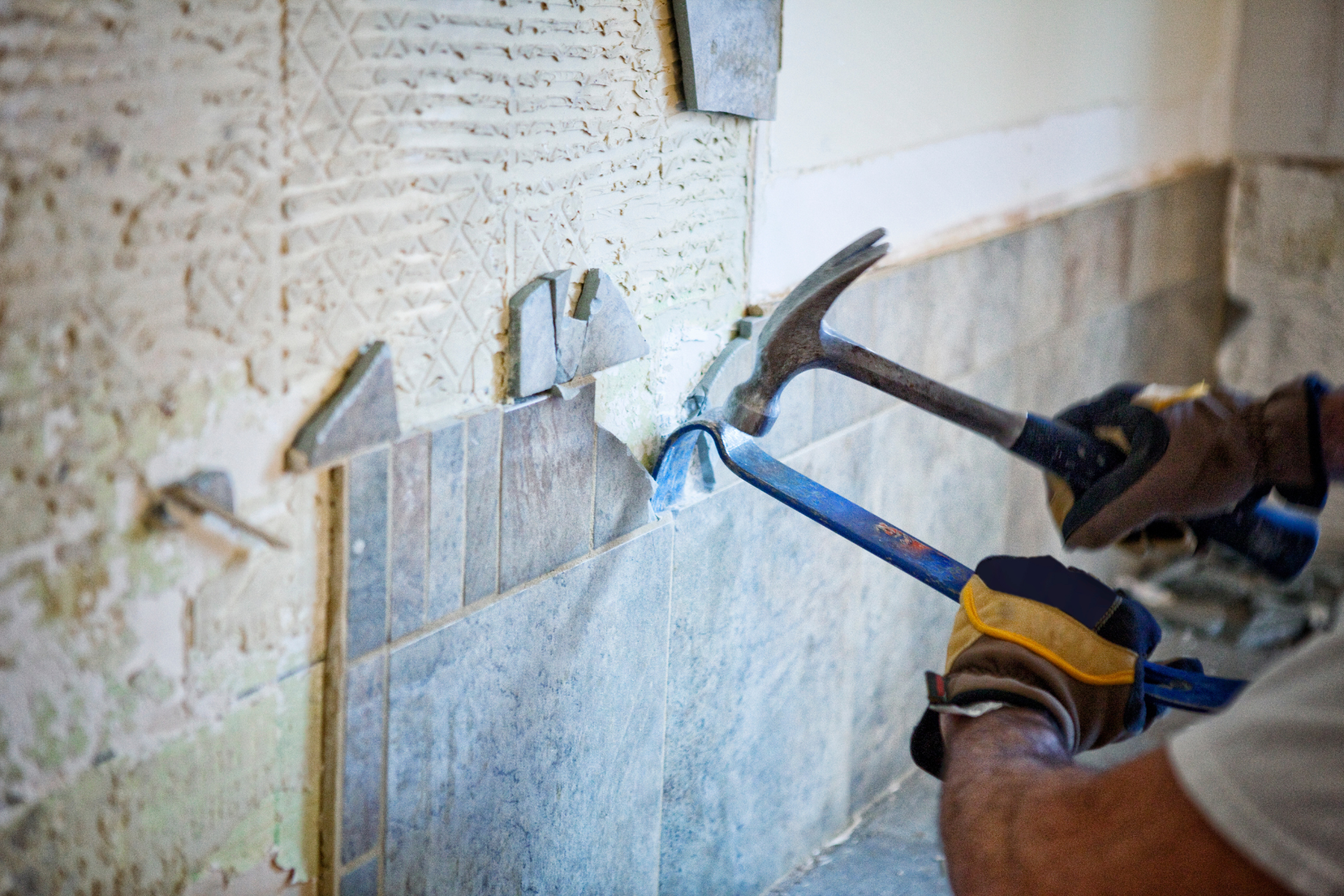 A man is using a hammer to remove tiles from a wall.