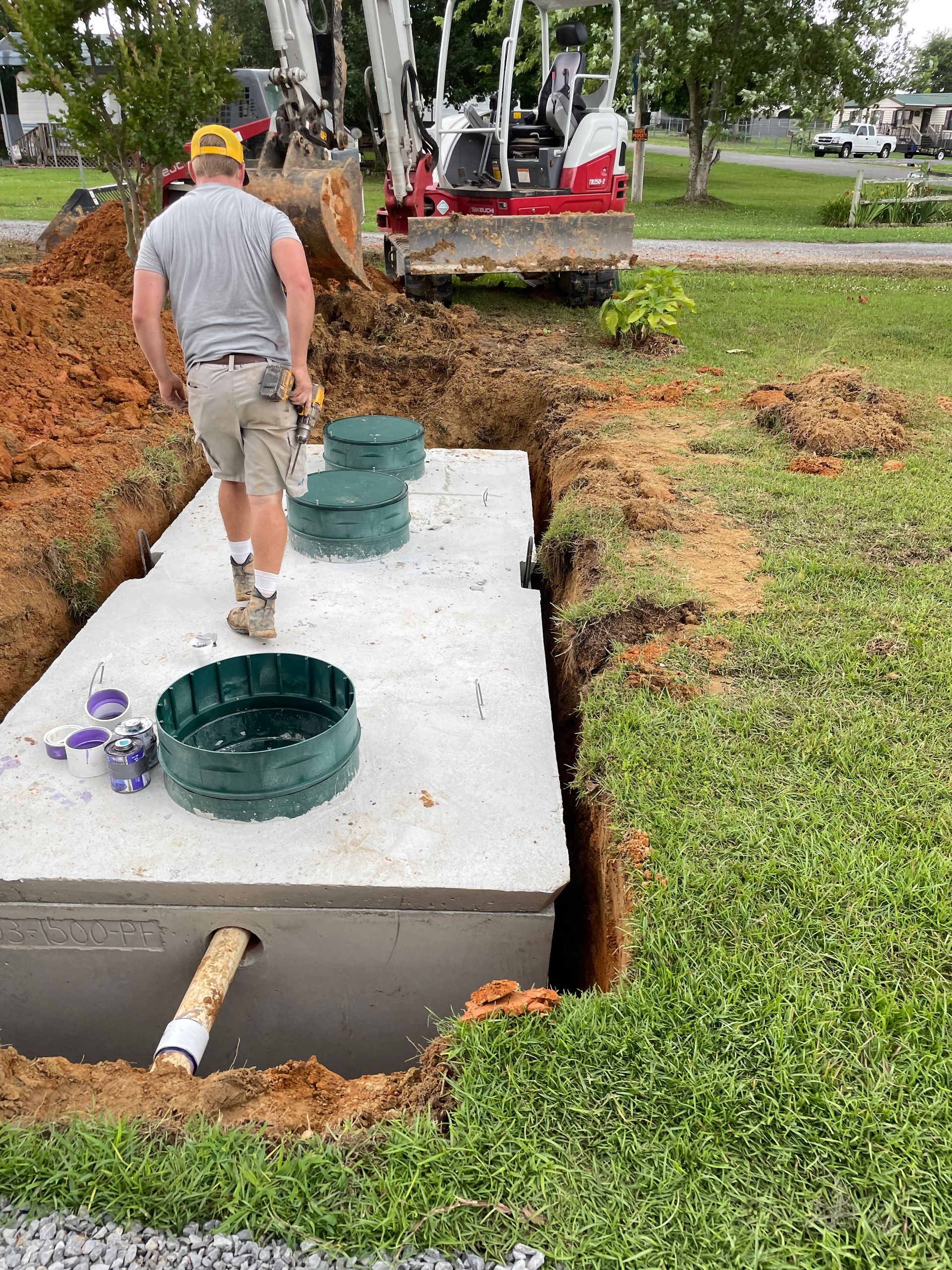 A man is standing in the dirt next to a septic tank.