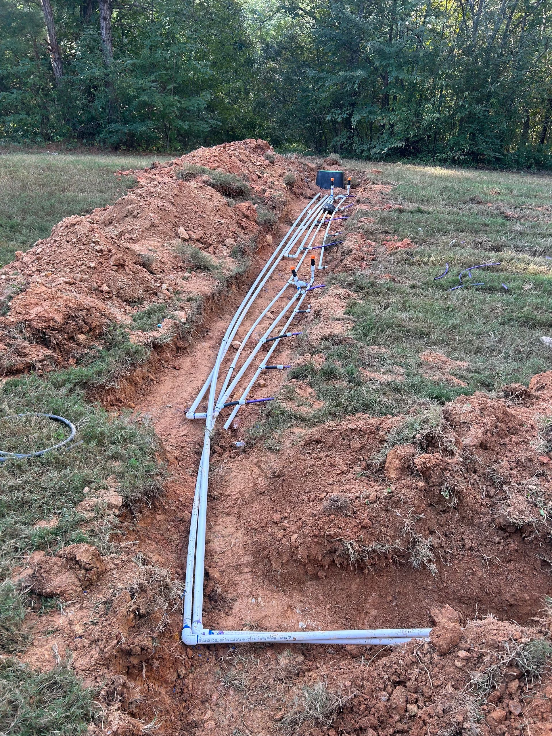 A bunch of pipes are laying in the dirt in a field.