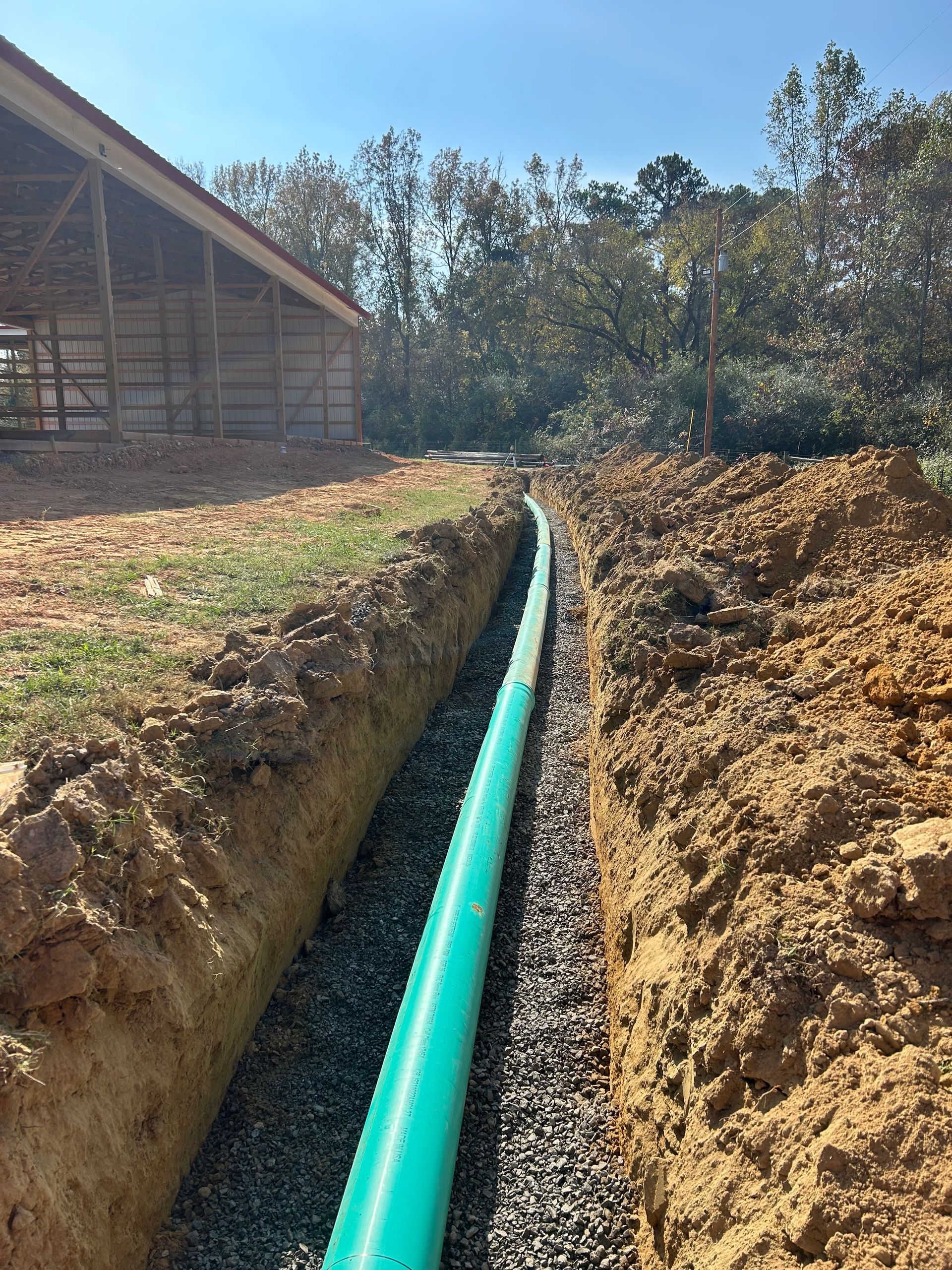 A green pipe is being installed in the dirt next to a building.