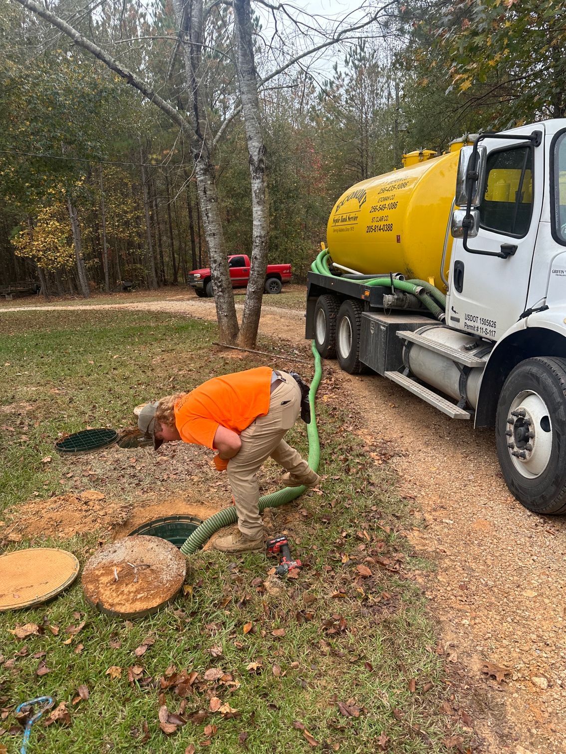 A man is kneeling in front of a septic tank next to a truck.