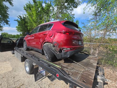 A damaged red Kia Sportage SUV sits secured on a flatbed tow truck outdoors.