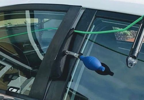 A blue air pump wedge is inserted between a car door and its frame to create a gap for unlocking the vehicle.