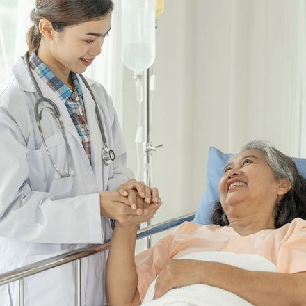 A doctor is holding the hand of a patient in a hospital bed.