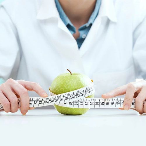 A woman is measuring an apple with a tape measure.