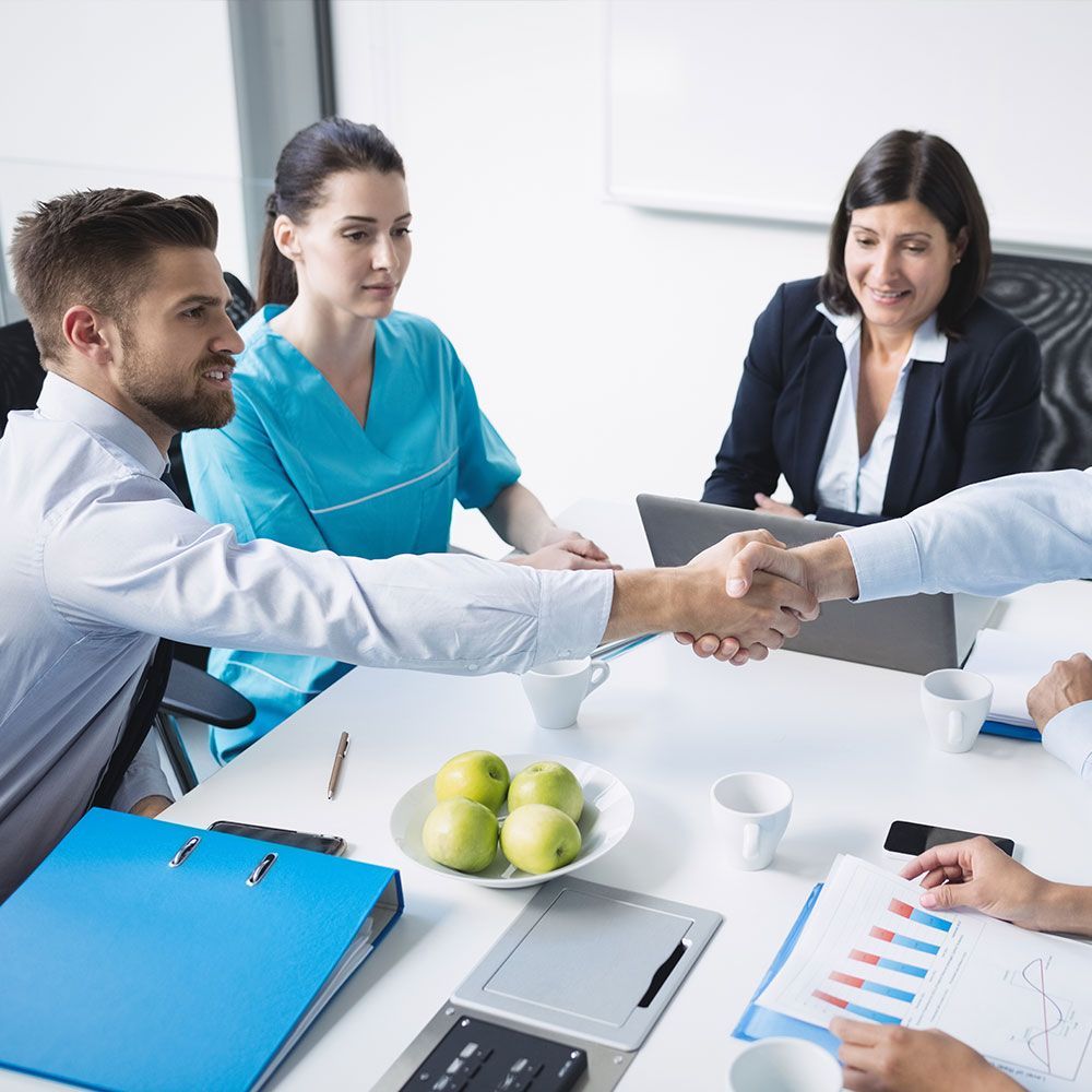 A group of people are sitting around a table shaking hands.