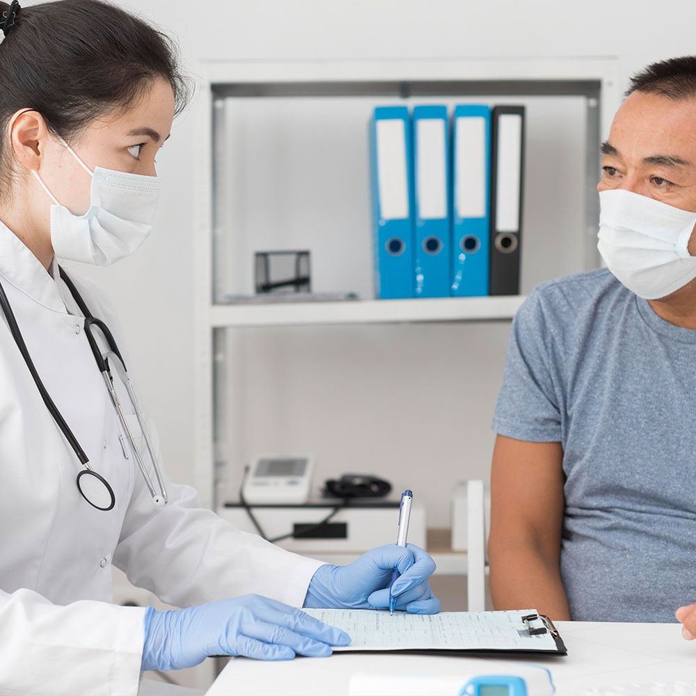 A doctor is wearing a mask and gloves while talking to a patient.